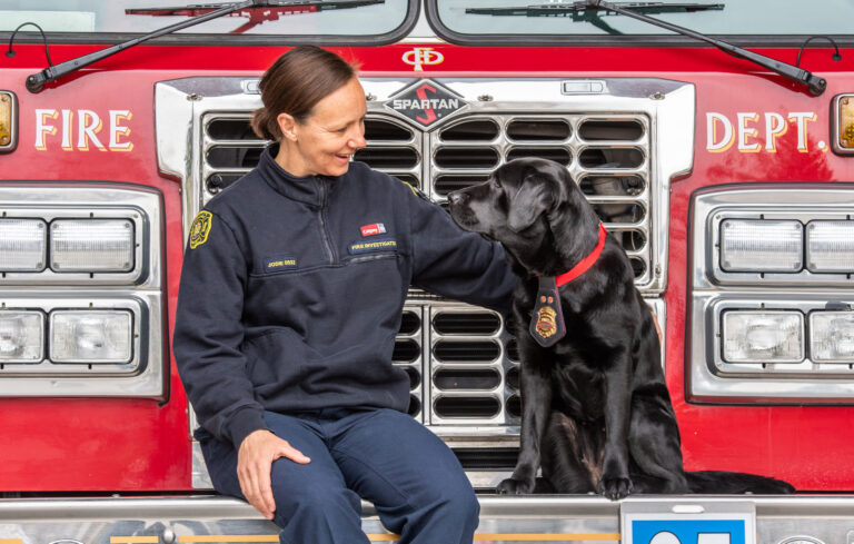 Calgary Fire Department fire investigator Jodie Grisdale with ignitable liquid detection canine Willow in front of a fire truck.