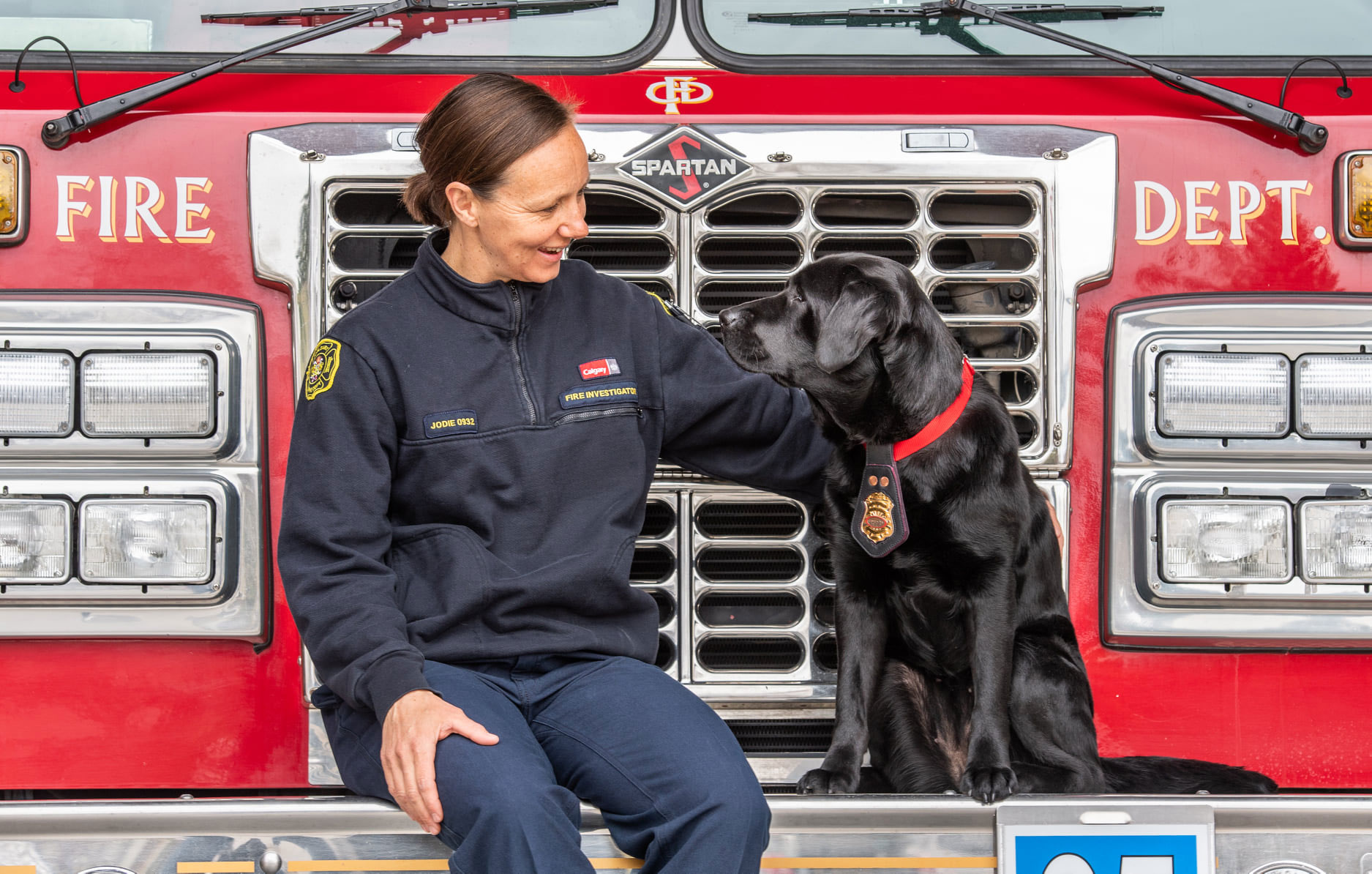 Calgary Fire Department fire investigator Jodie Grisdale with ignitable liquid detection canine Willow in front of a fire truck.